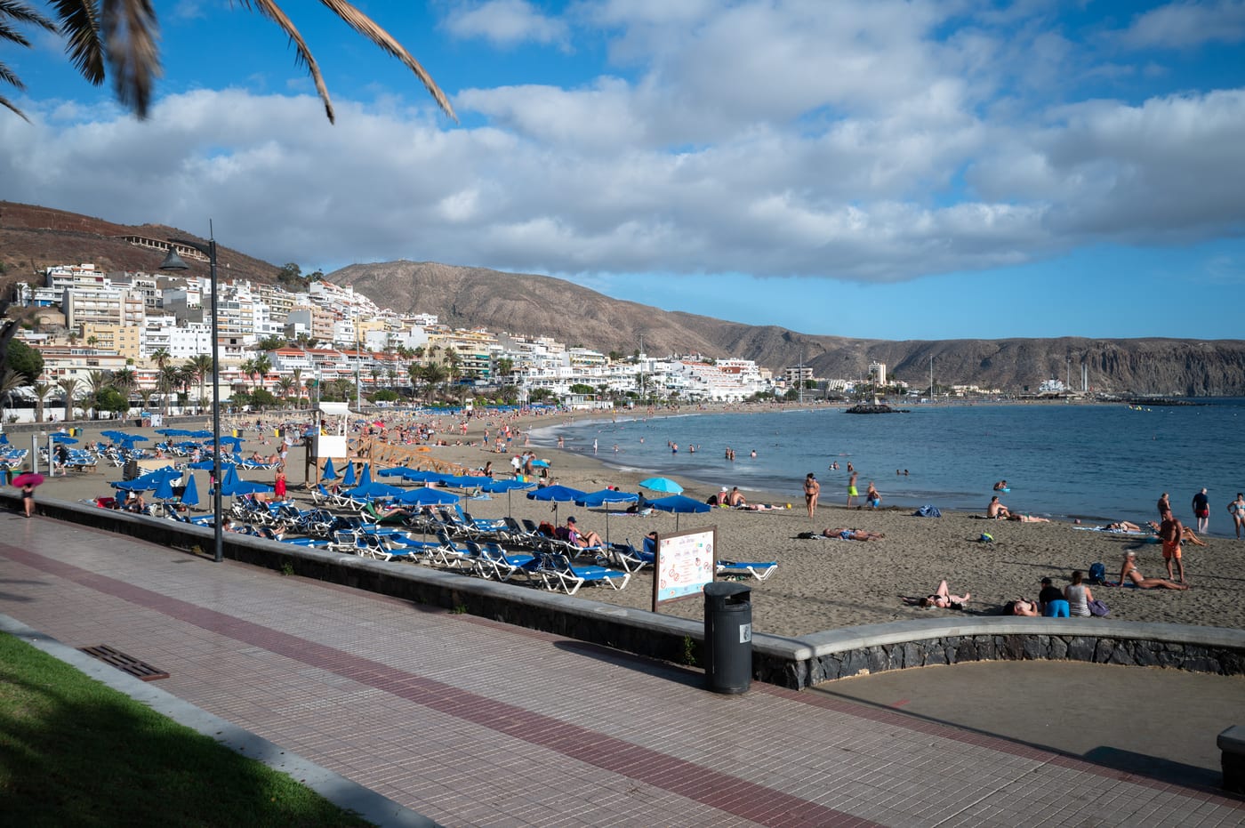 Vista amplia de la arena dorada de la Playa de las Vistas en Los Cristianos (Arona), con la bahía, el pueblo y las montañas al fondo.