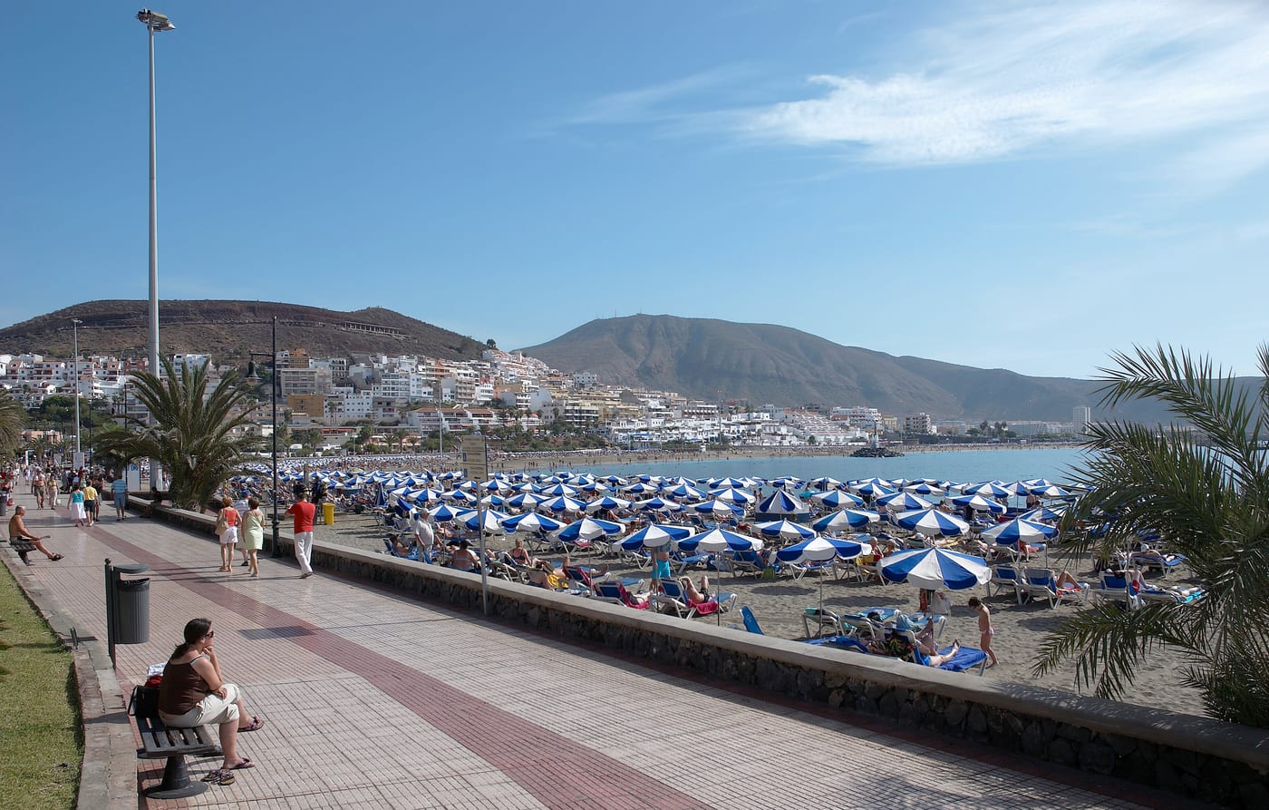 Playa de Los Cristianos con sus hamacas y sombrillas, el paseo marítimo y la montaña de Guaza al fondo (Arona, Tenerife).
