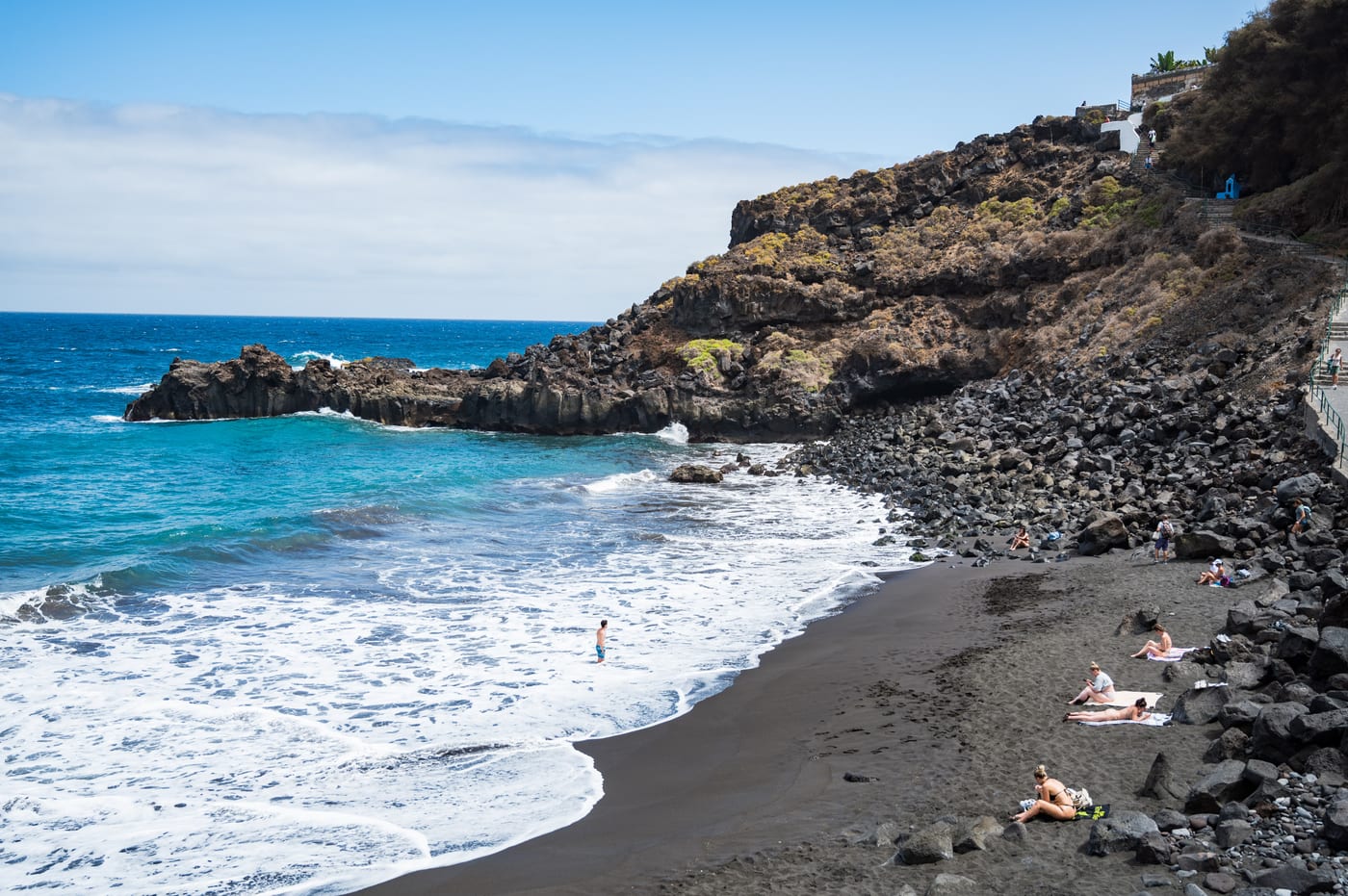 La Playa del Bollullo a pie de orilla, con su arena negra y los acantilados con plataneras que la rodean.