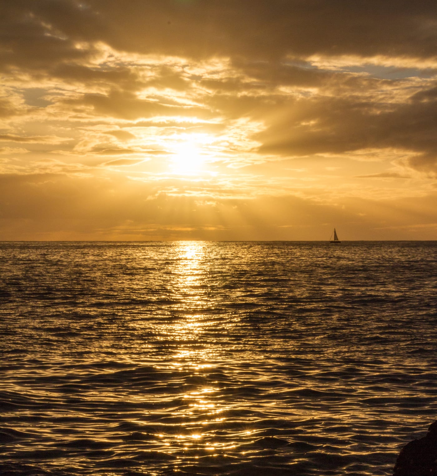 Yate de vela en el horizonte del Atlántico al atardecer en Tenerife, recortado contra el reflejo dorado del sol sobre el agua.