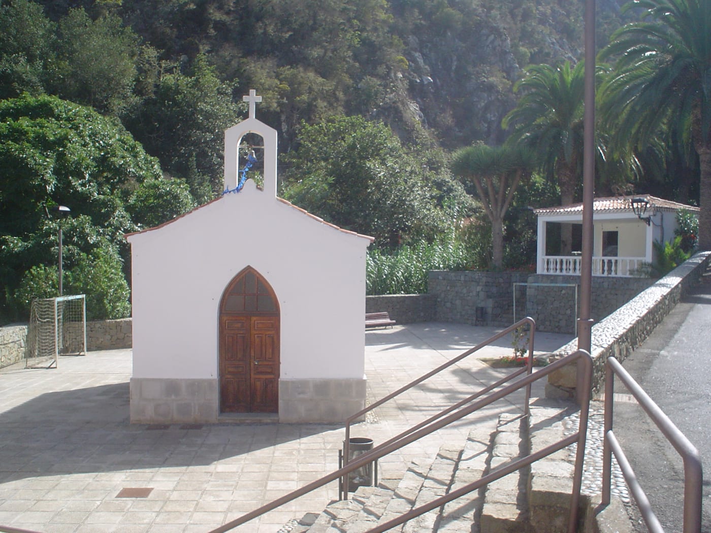 La ermita y plaza de Chamorga, con palmeras y un drago tras la pequeña capilla blanca.